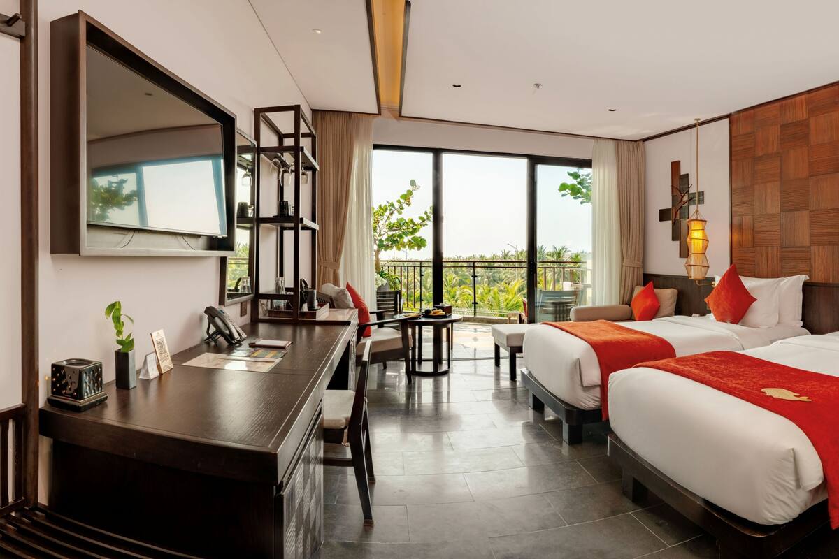 A hotel room with two beds, a desk, a chair, a large window, and a balcony.