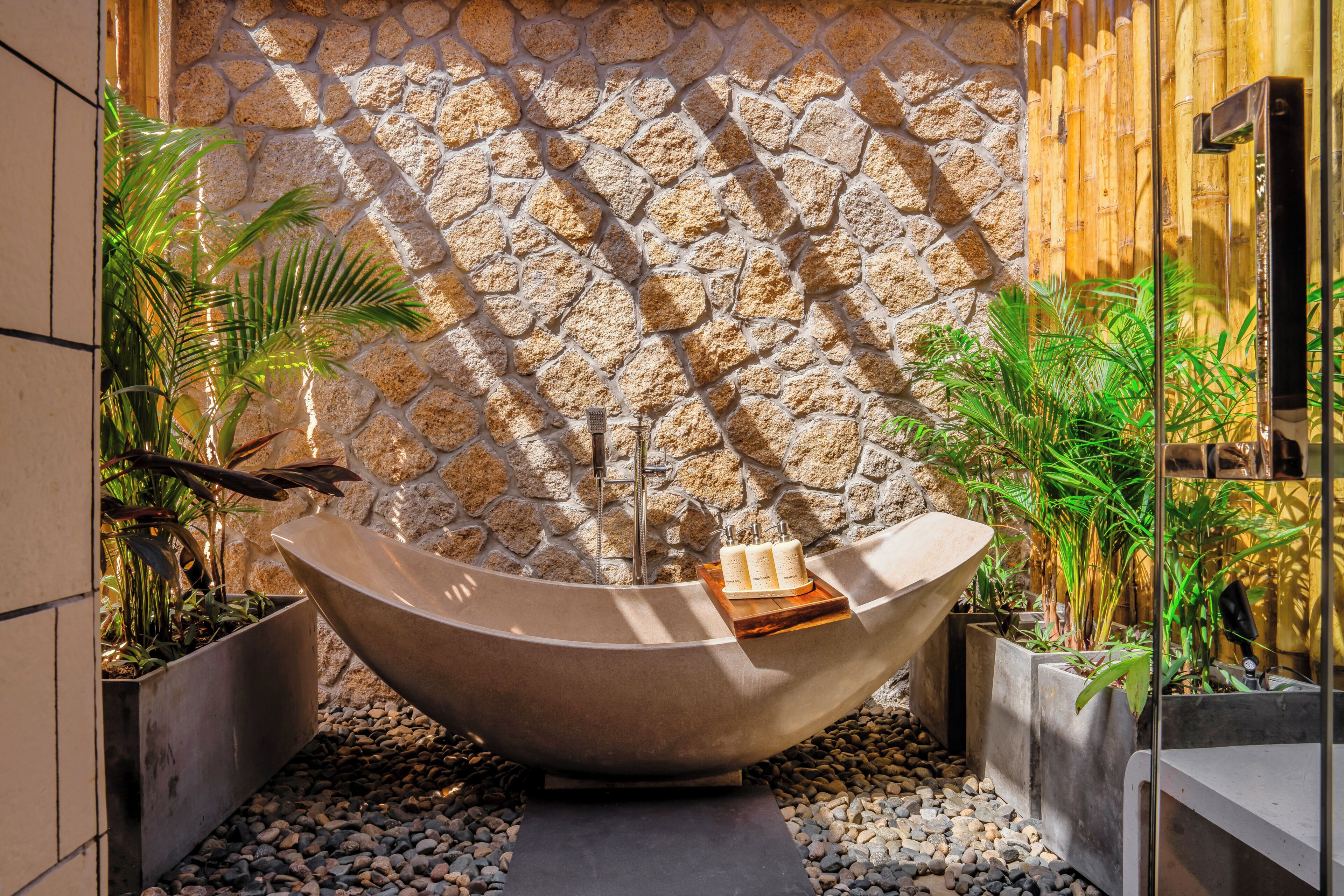 Un espacio de spa con una bañera grande independiente, paredes de piedra y plantas en macetas.