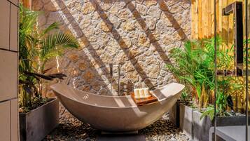 Un espacio de spa con una bañera grande independiente, paredes de piedra y plantas en macetas.