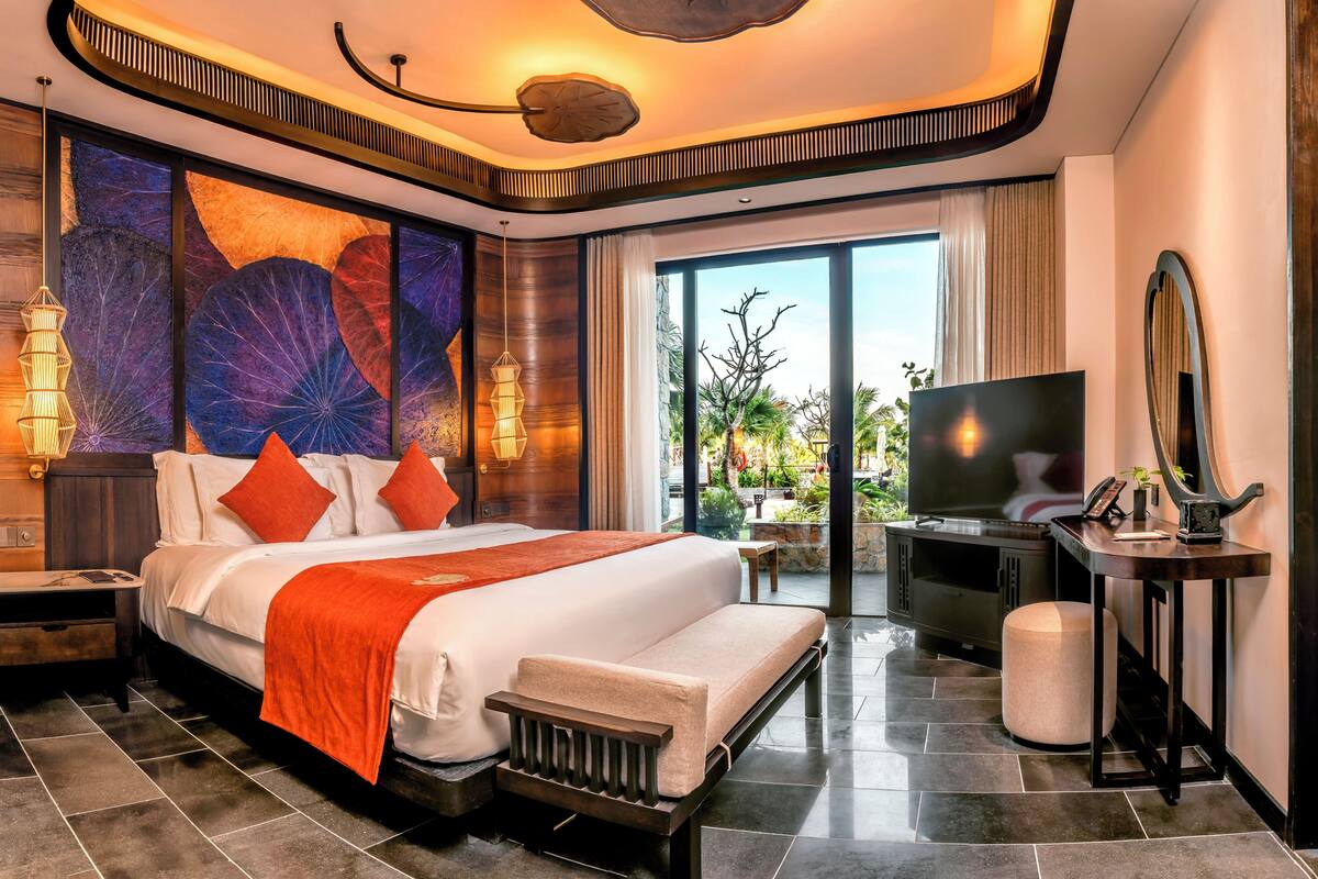 A modern hotel room with a large bed, a TV, a desk, and a balcony with a view.