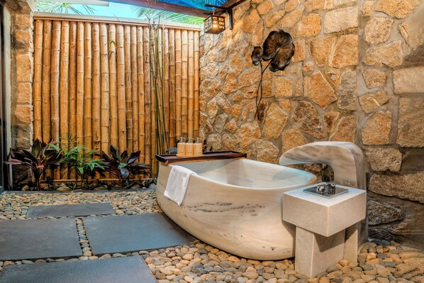 A spa area with a stone wall, a bamboo fence, and a marble bathtub. - Amiana Resort Cam Ranh (Cam Lam)