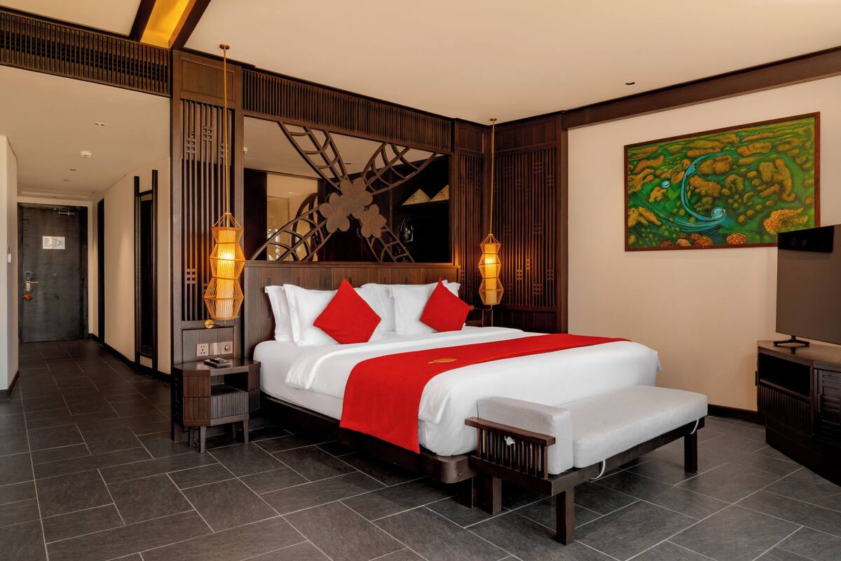 A hotel room with a large bed, a nightstand, a TV, and a painting on the wall.