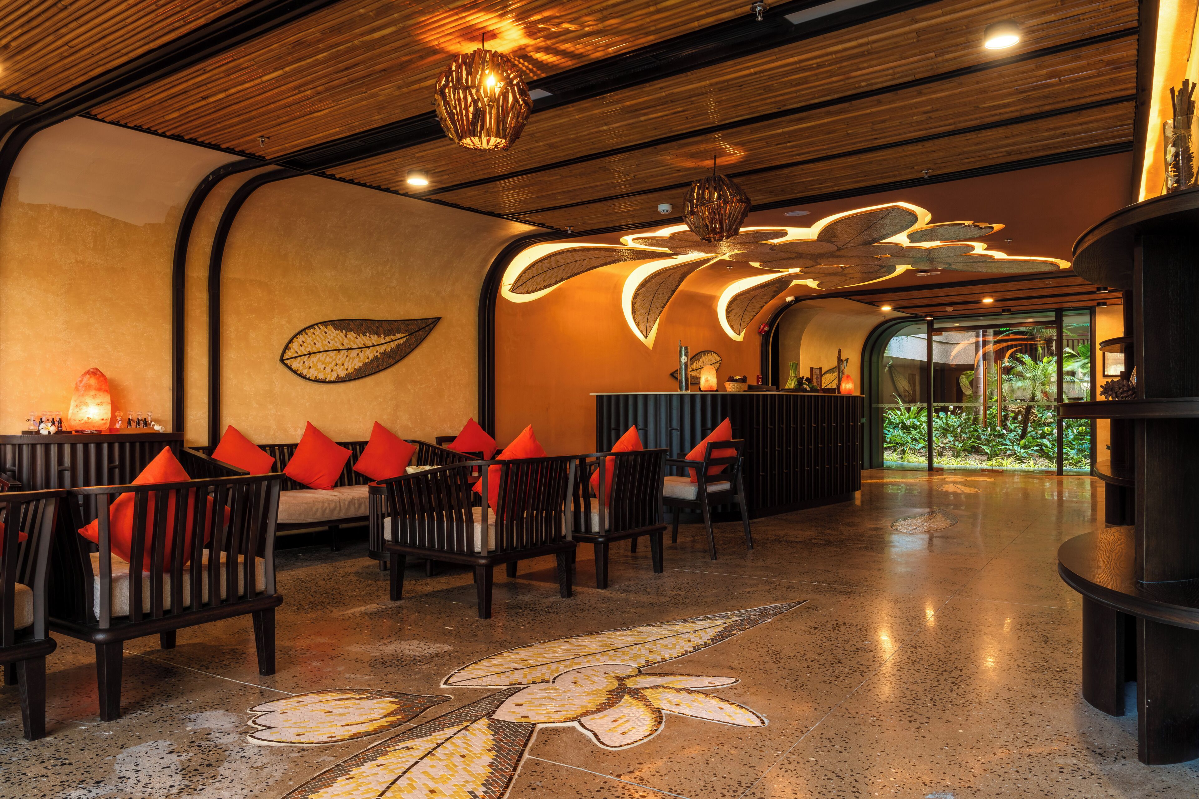 An indoor space with wooden ceiling beams, a patterned floor, and seating with orange cushions.