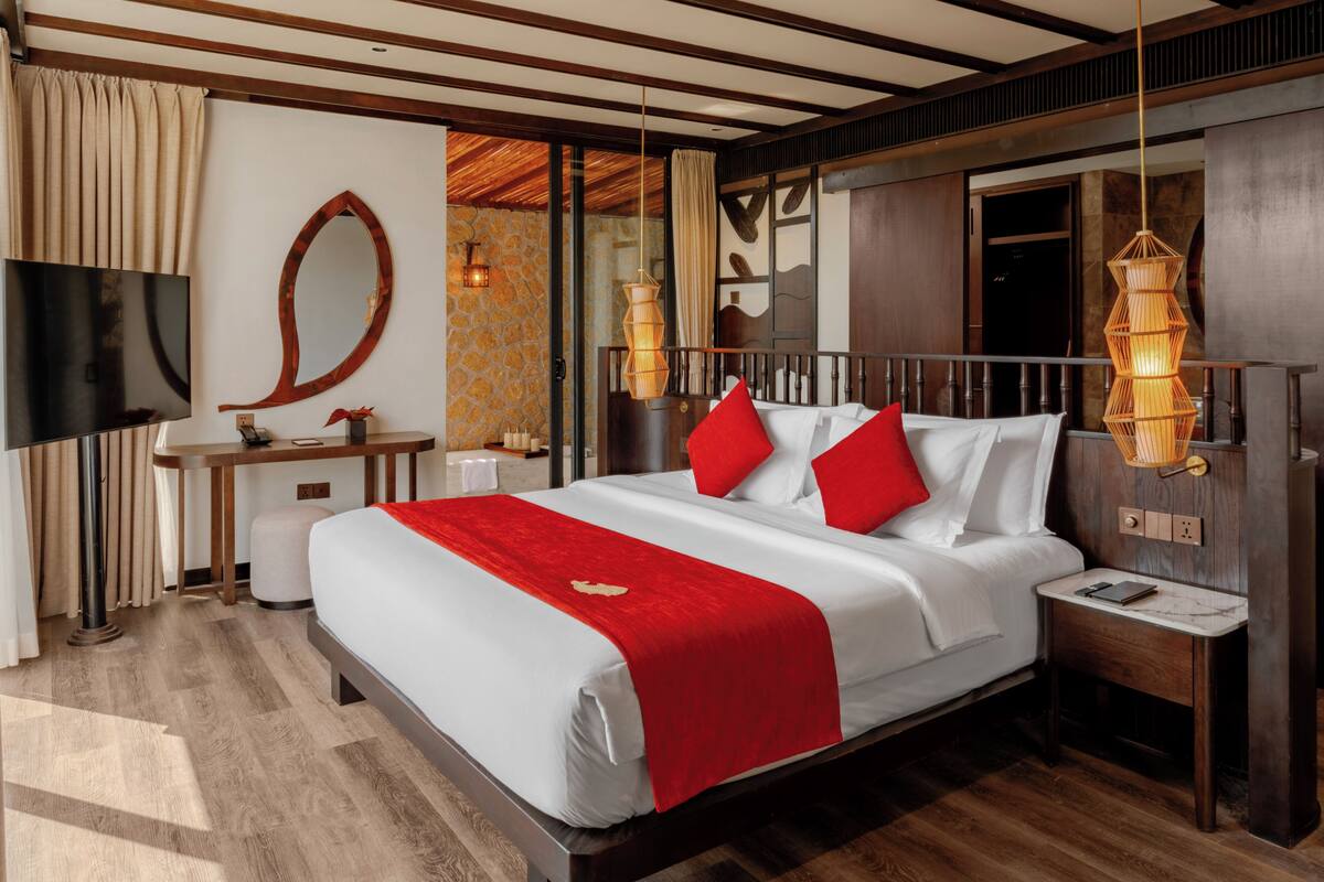 A hotel room with a large bed, a TV, a desk, and a mirror.