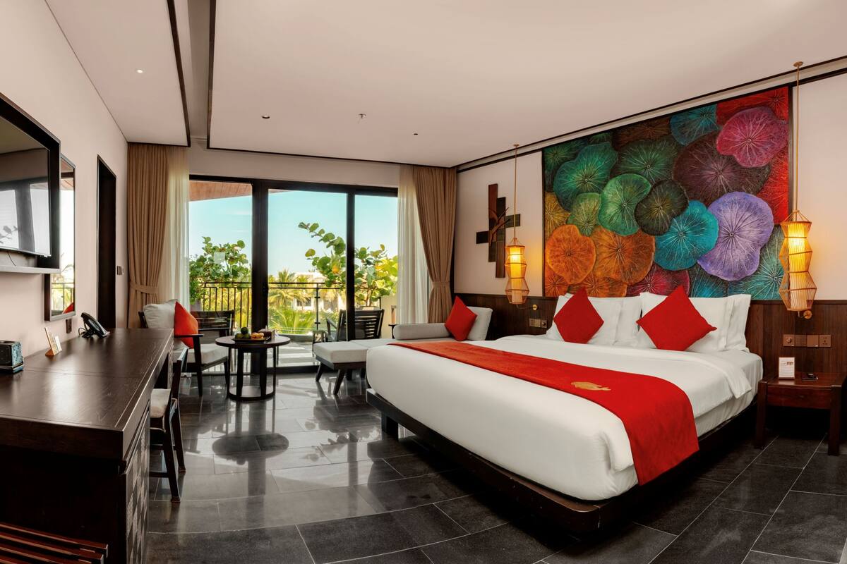 A modern hotel room with a large bed, a desk, a chair, a balcony with plants, and a colorful wall mural.