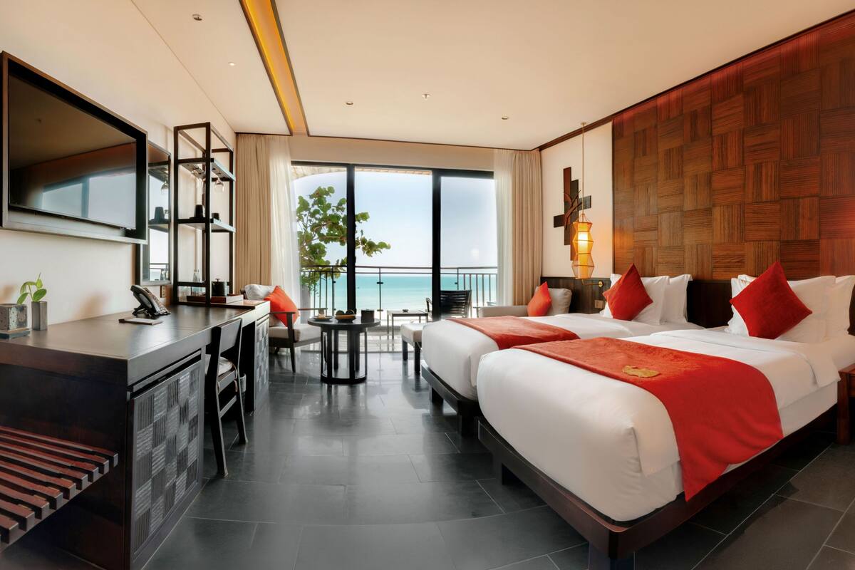 A hotel room with a large bed, a desk, a TV, and a view of the sea.