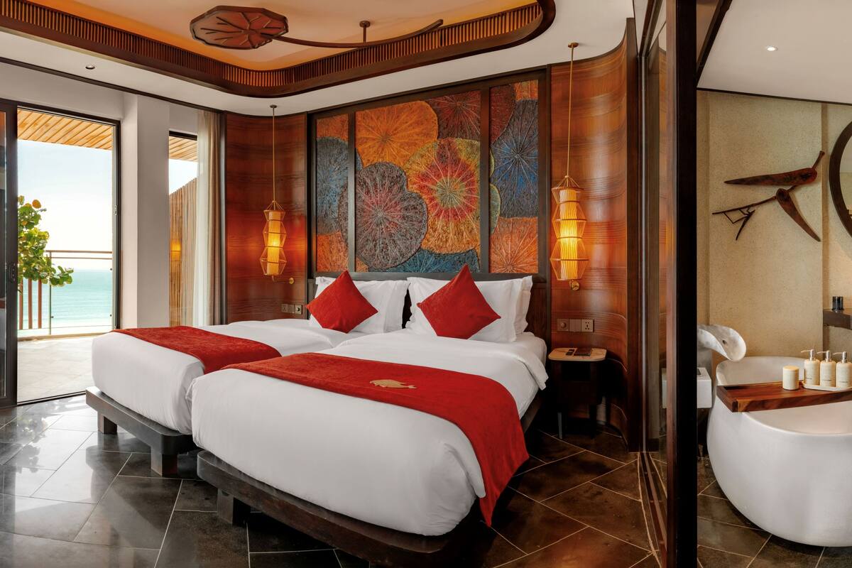 A hotel room with a large bed, two bedside tables, a bathroom with a bathtub, and a view of the sea.