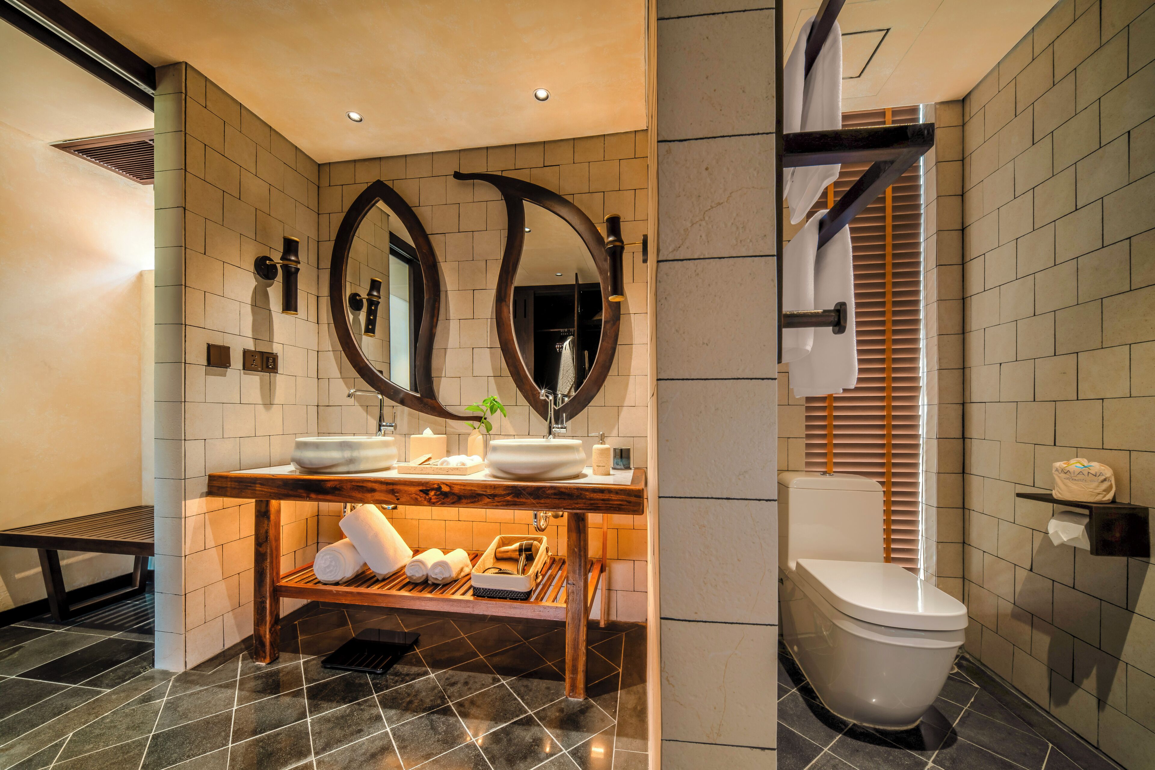 A modern bathroom with a wooden vanity, two mirrors, a toilet, and a bench.