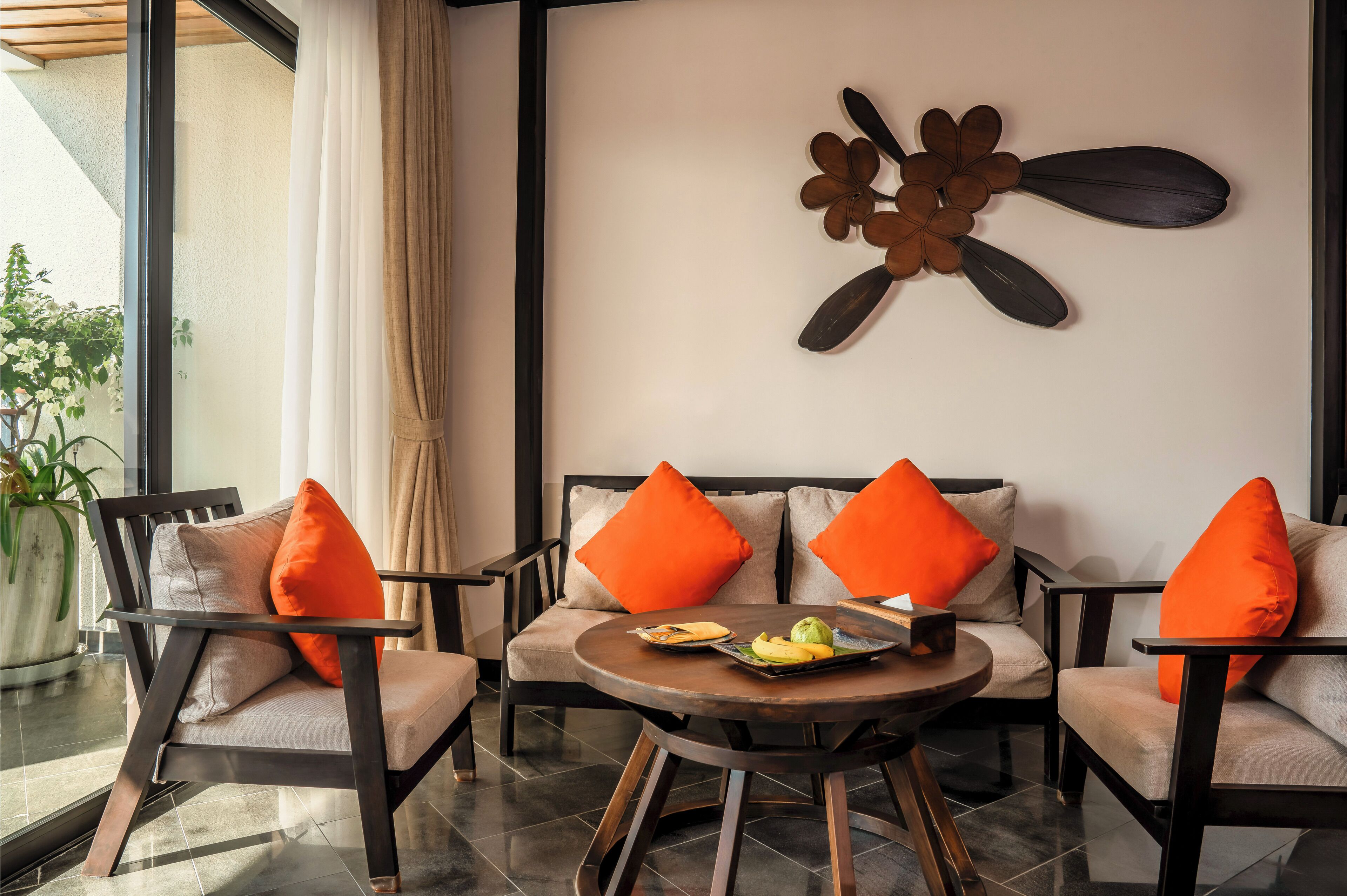 Una habitación moderna con un conjunto de sofás, una mesa redonda con fruta y un abanico decorativo en la pared.