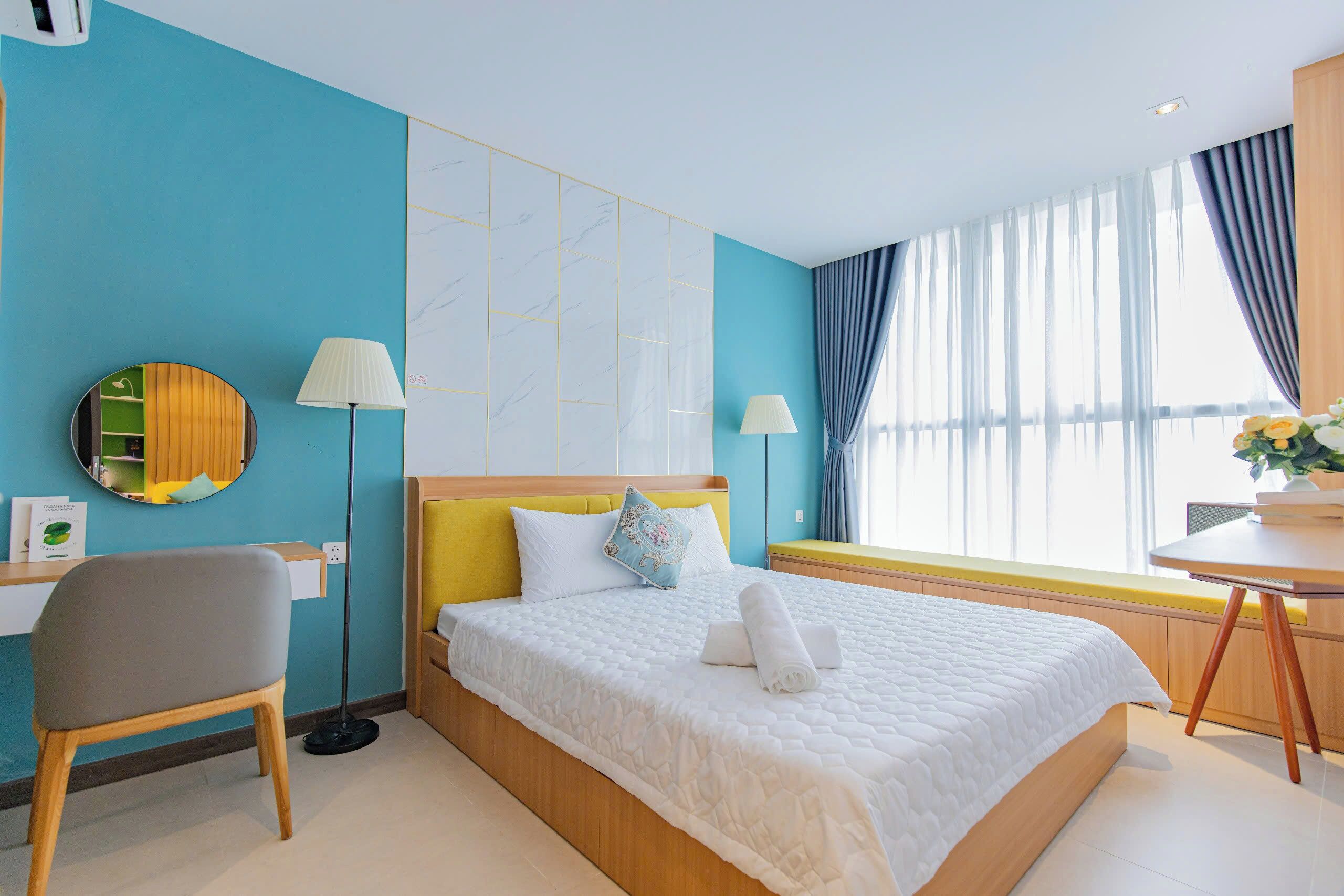 Ein Hotelzimmer mit Bett, Schreibtisch, Stuhl, Lampe und einem fenster mit Vorhängen.