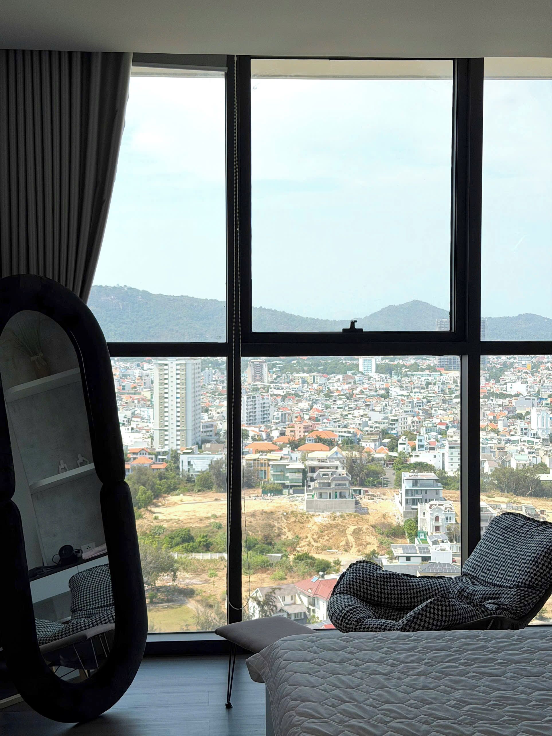 Un dormitorio con un ventanal grande, una cama, una silla y un espejo.