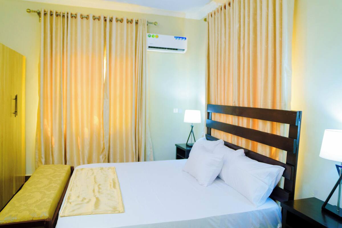 Une chambre d’hôtel équipée d’un lit, de rideaux, d’un appareil de climatisation et d’une table de chevet avec une lampe.