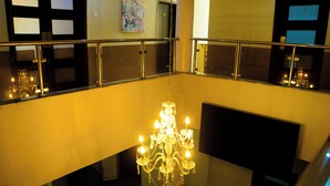 A chandelier in a lobby with a glass railing and a painting on the wall. - Consulate Hotel (Ibadan)