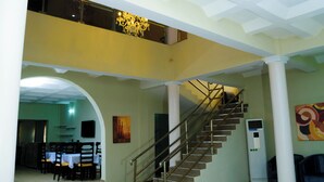 A spacious interior with a staircase leading to an upper level, a dining area with tables and chairs, and a modern air conditioning unit. - Consulate Hotel (Ibadan)