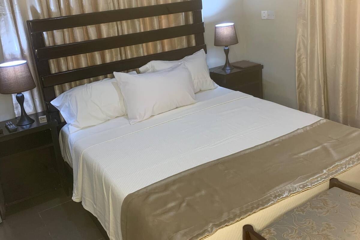 Un lit bien fait, avec une tête de lit en bois, une lampe de chevet et une table de chevet sur laquelle se trouve une télécommande.