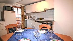 A compact kitchen with white cabinets, a microwave, a stove, and a sink. There is a dining table set with plates, glasses, and cutlery. - Apartment Plank by Interhome (Kaltenbach)