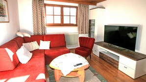 A living room with a red sofa, a wooden coffee table, a TV, and a red armchair. - Apartment Plank by Interhome (Kaltenbach)