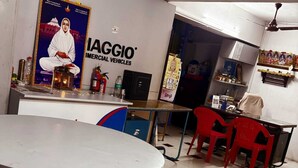 A restaurant interior with a round table, red chairs, a counter, and a wall with a poster. - GSR Stay Home (Puducherry)
