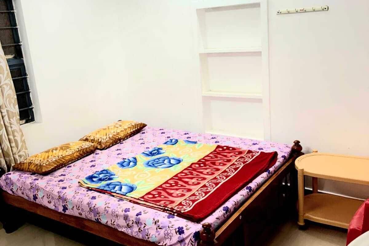 A bedroom with a bed, a ceiling fan, a window with curtains, a bedside table, and a wall-mounted shelf.