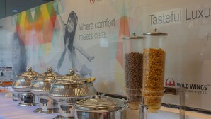 A buffet setup with multiple food containers and a promotional banner in the background. - WILDWINGS PREMIUM HOTEL (Hyderabad)