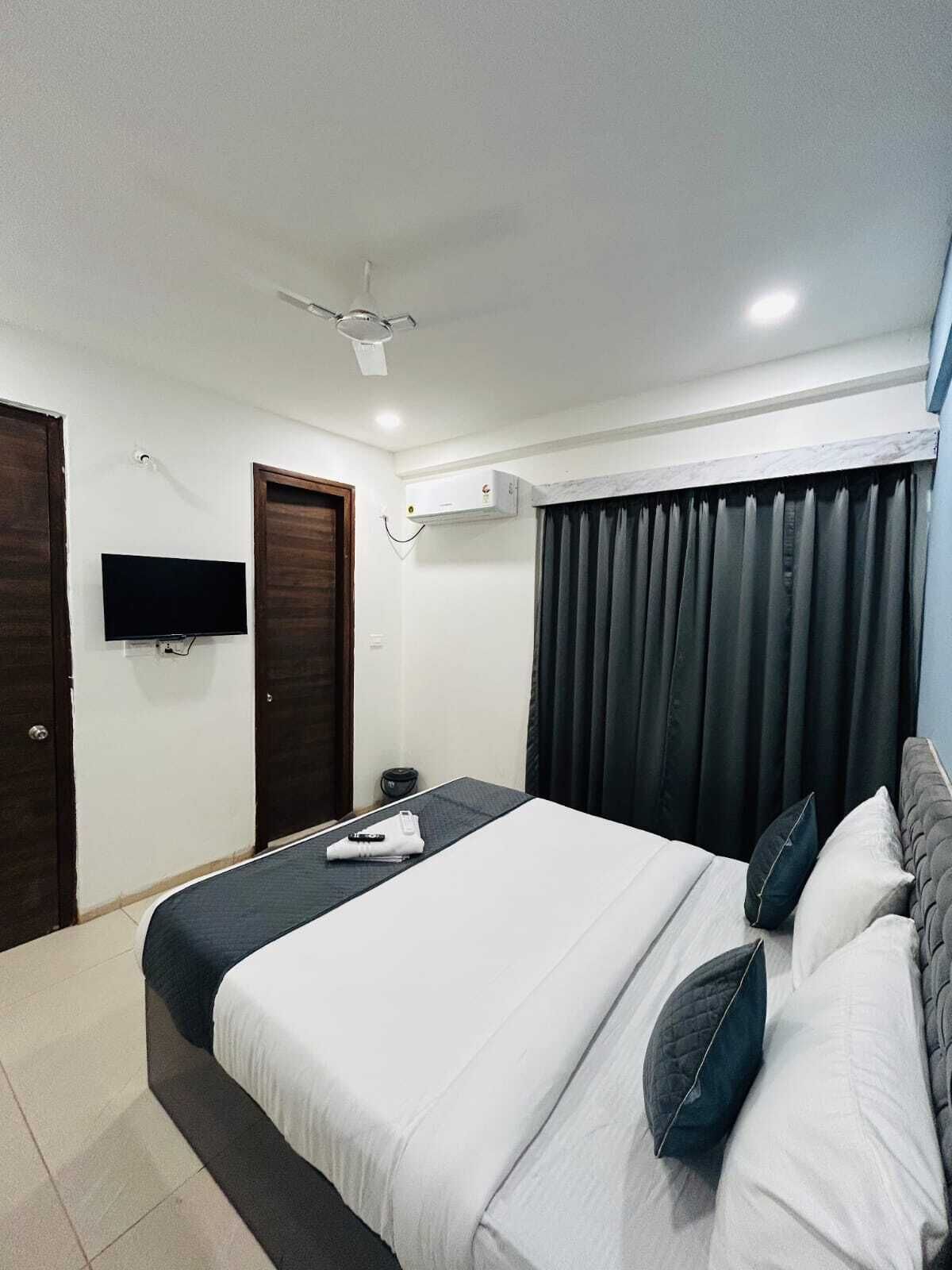 A hotel room with a bed, a ceiling fan, an air conditioning unit, a TV, and a window with curtains.