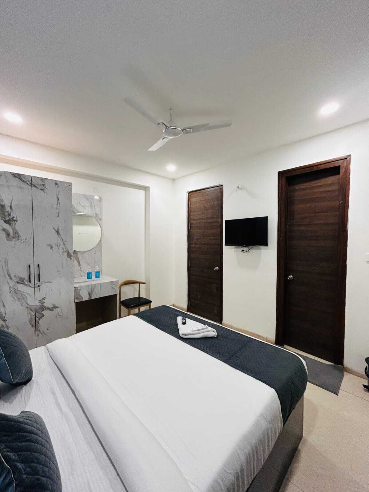 A hotel room with a bed, a wardrobe, a desk with a mirror, a TV, and two doors.