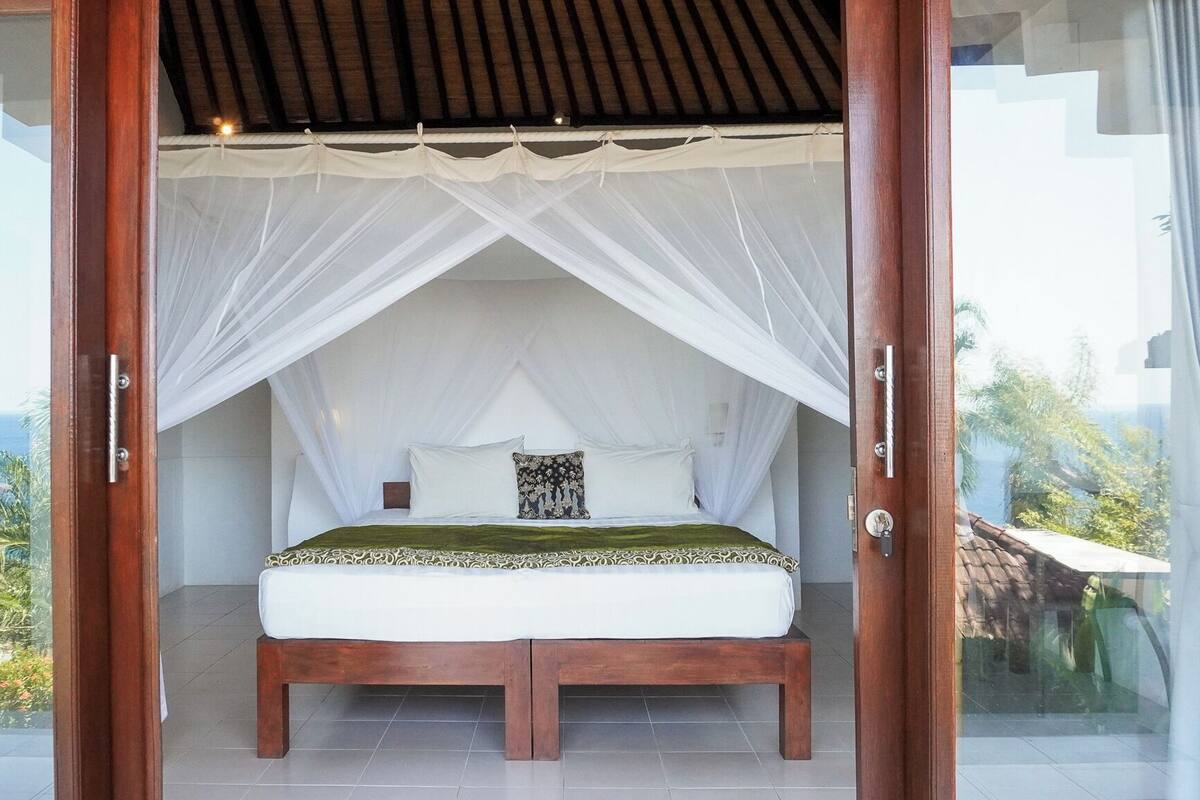 Quarto com cama de dossel, vista para o exterior e varanda.