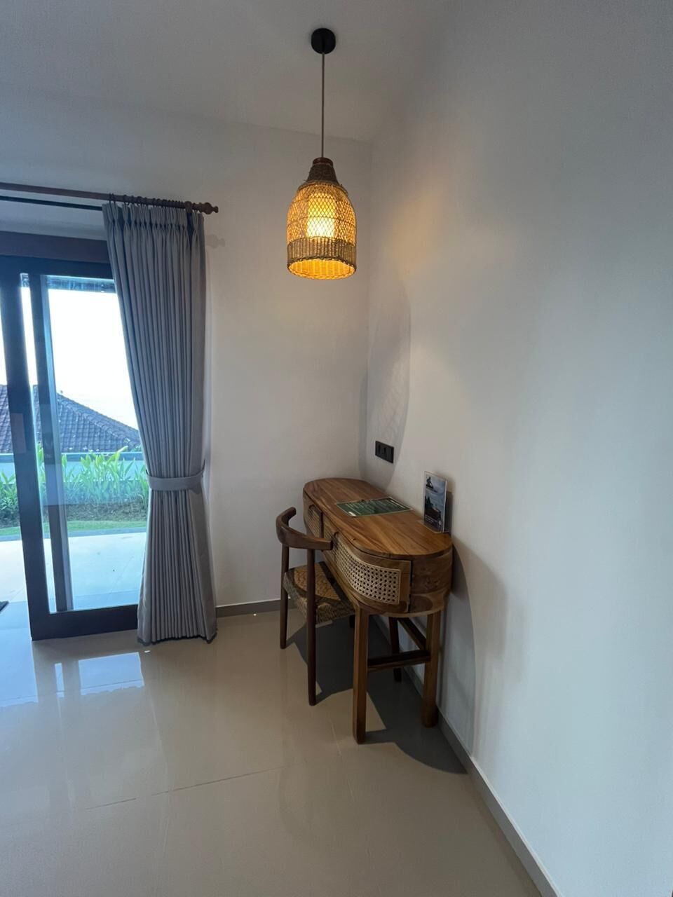 A room with a wooden table and chairs, a hanging light fixture, and a view through a glass door.