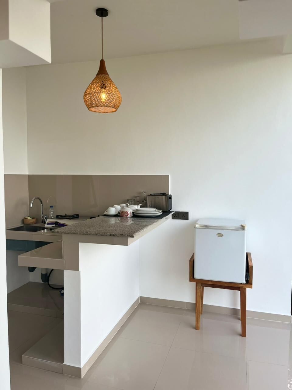 Een compacte keuken met een inbouwkookeiland, een witte koelkast en een hangende pendelverlichting.