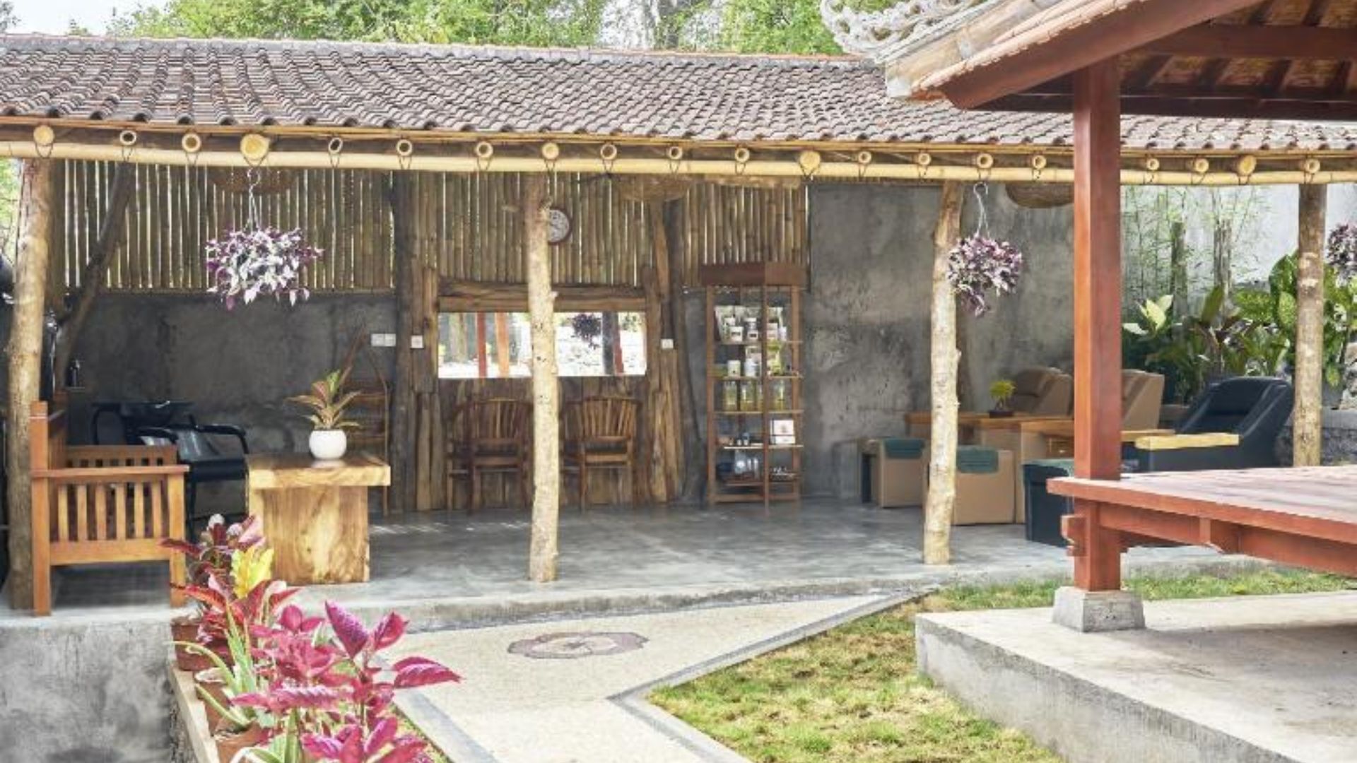A rustic outdoor seating area with bamboo walls, a concrete floor, and a pergola with hanging plants.