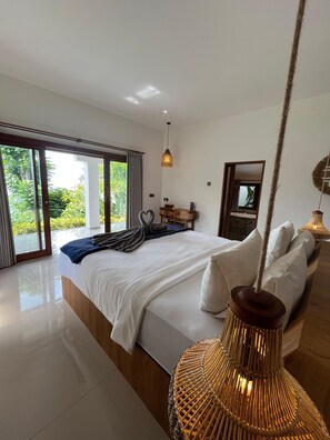 Un dormitorio moderno con una cama grande, una lámpara colgante y vistas a la vegetación por la ventana.