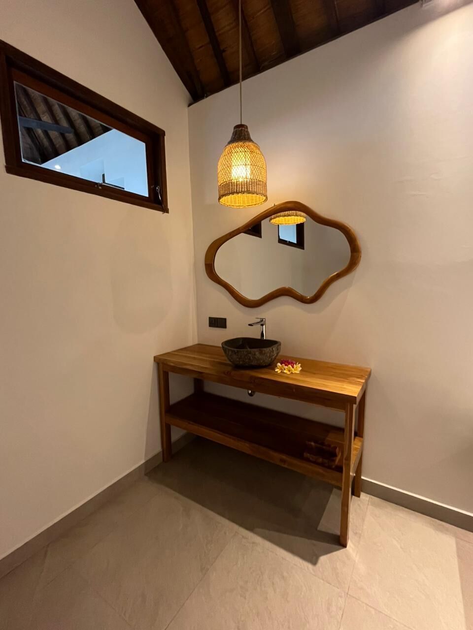 Un bagno con un mobile vanitario in legno, un lavabo a incasso, uno specchio con cornice decorata e una lampada a sospensione.