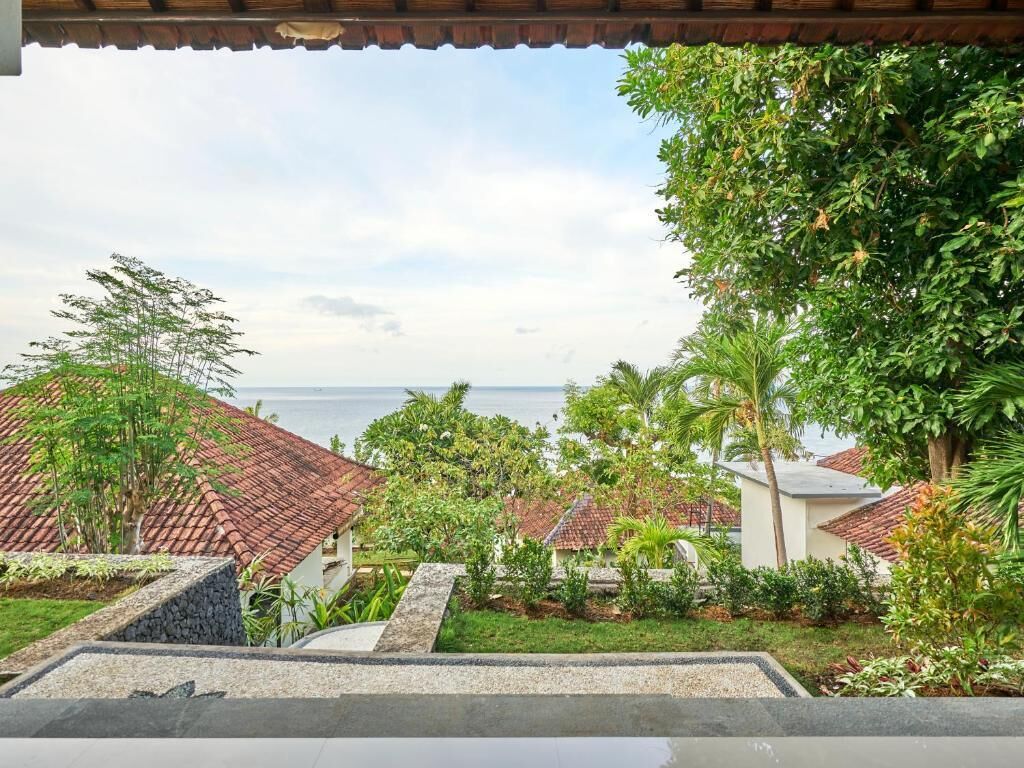 A coastal property with a view of the sea, featuring a garden with various plants and a tiled roof.