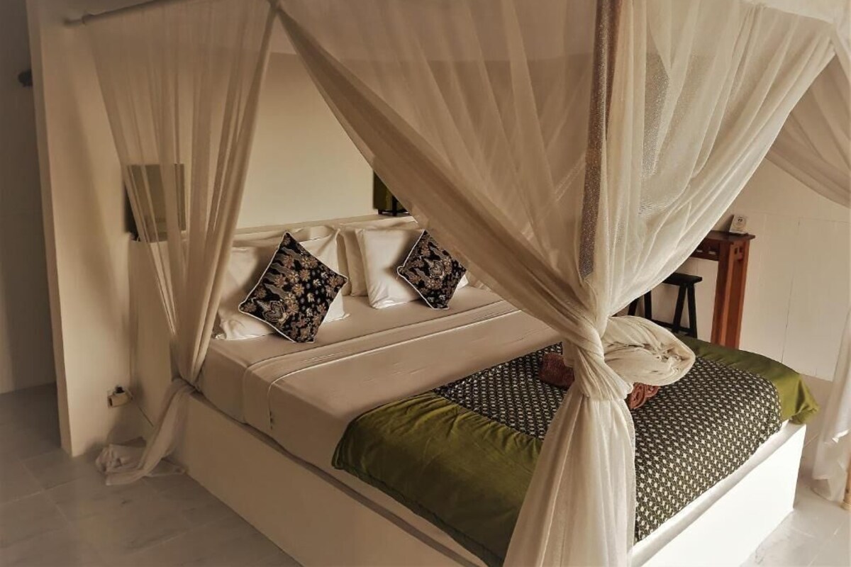 A bed with a canopy, pillows, and a green blanket.