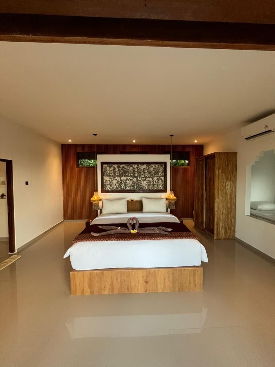 A spacious bedroom with a large bed, wooden headboard, and a wall-mounted artwork.