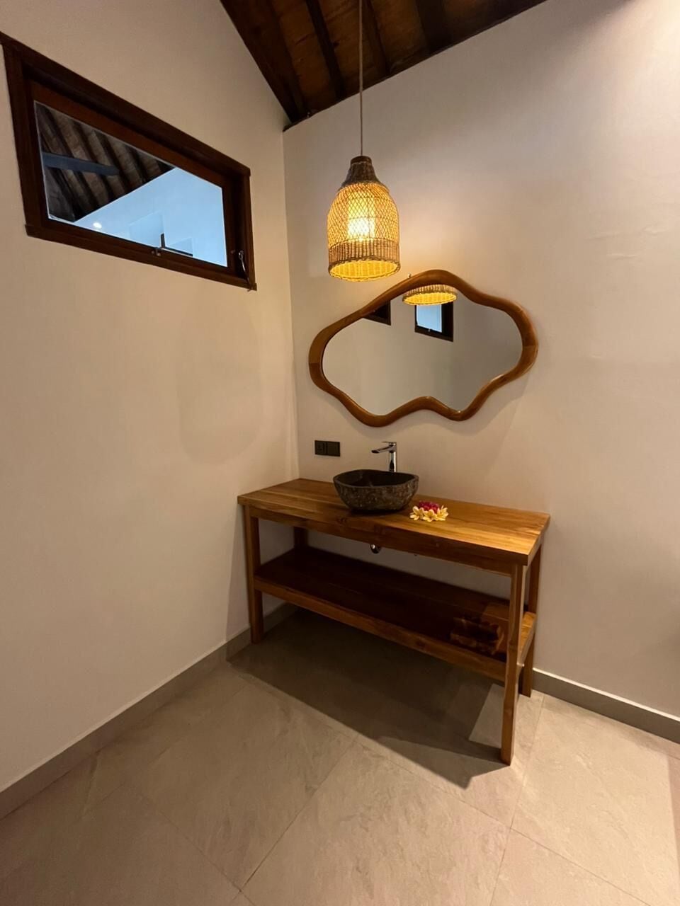 Casa de banho com toucador de madeira, espelho redondo e candeeiro suspenso.