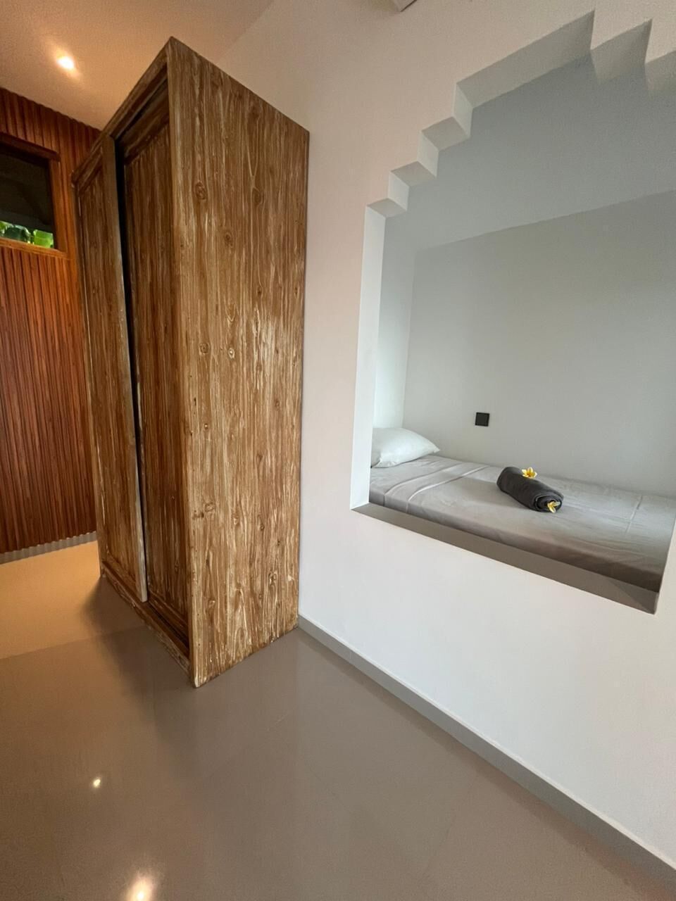 A modern room with a built-in bed, a wooden wardrobe, and a small window.