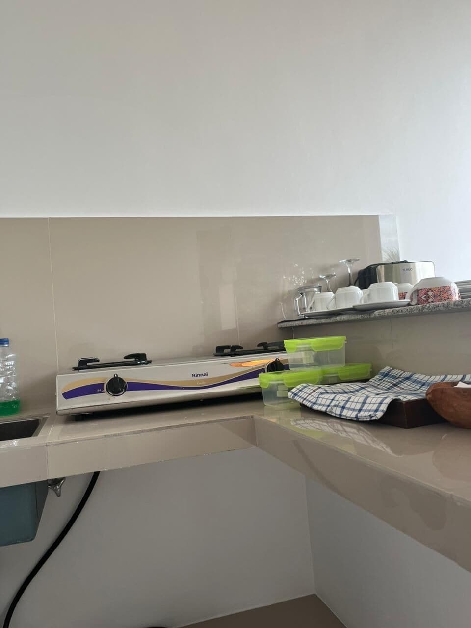 A kitchen with a gas stove, a water bottle, a dish rack, and a cloth.