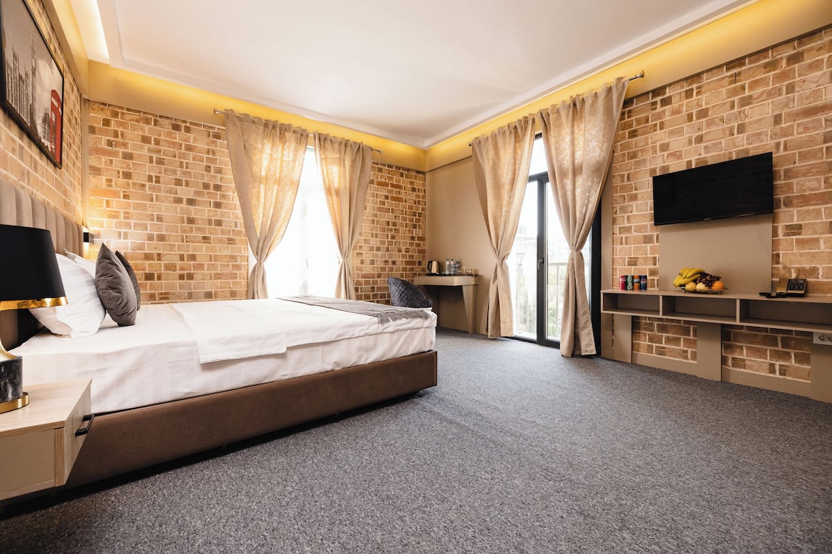 Habitación de hotel con pared de ladrillo, cama con ropa blanca, escritorio con televisor de pantalla plana y una pequeña zona de estar con un banco y una cafetera.