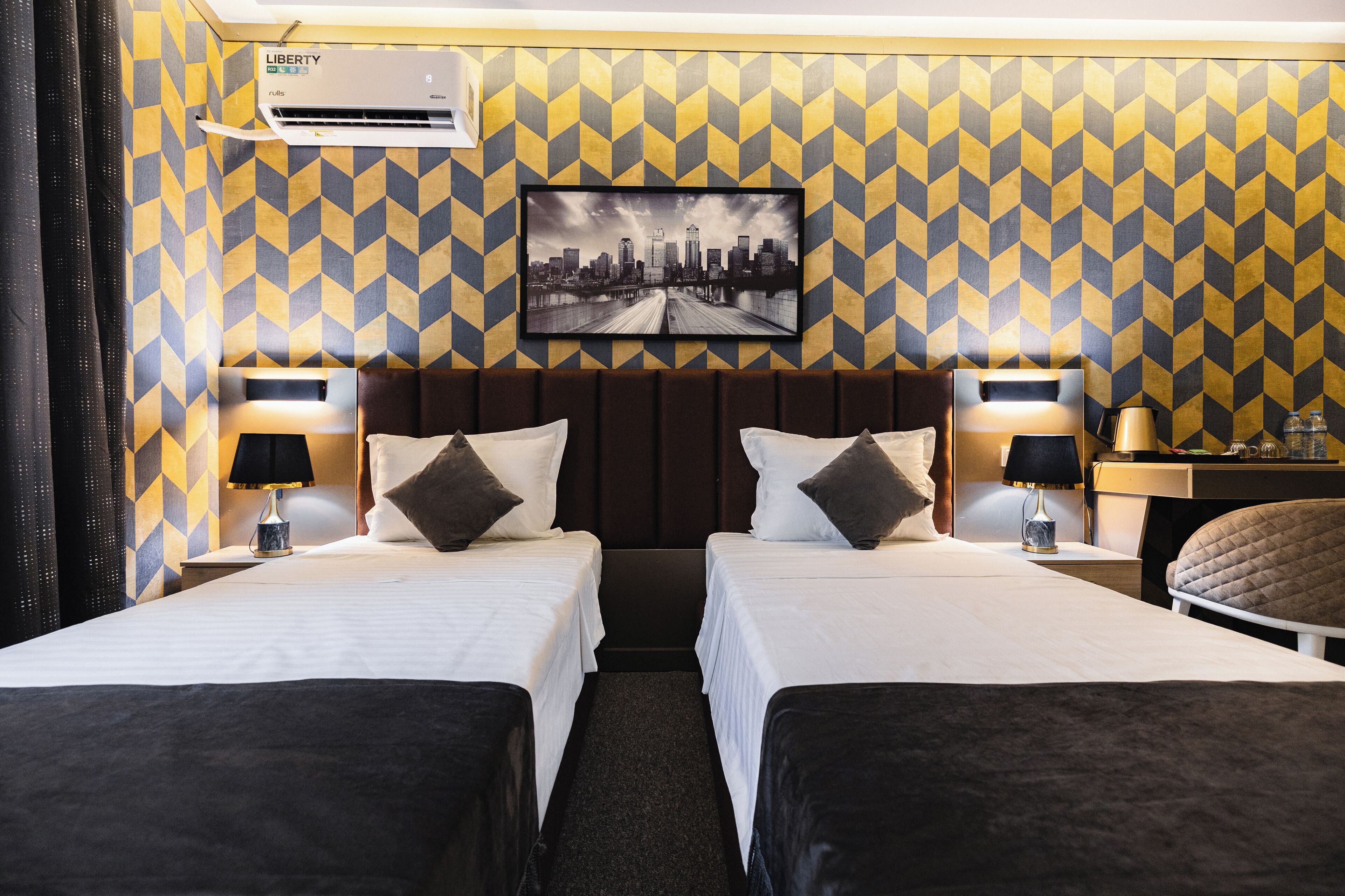 Ein Hotelzimmer mit zwei Betten, einem Stadtbild an der Wand und einer Klimaanlage.