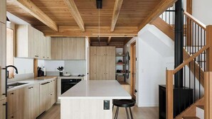 Eine moderne Küche mit Holzschränken, einer zentralen Kochinsel und einer Treppe mit Holzbalkon.