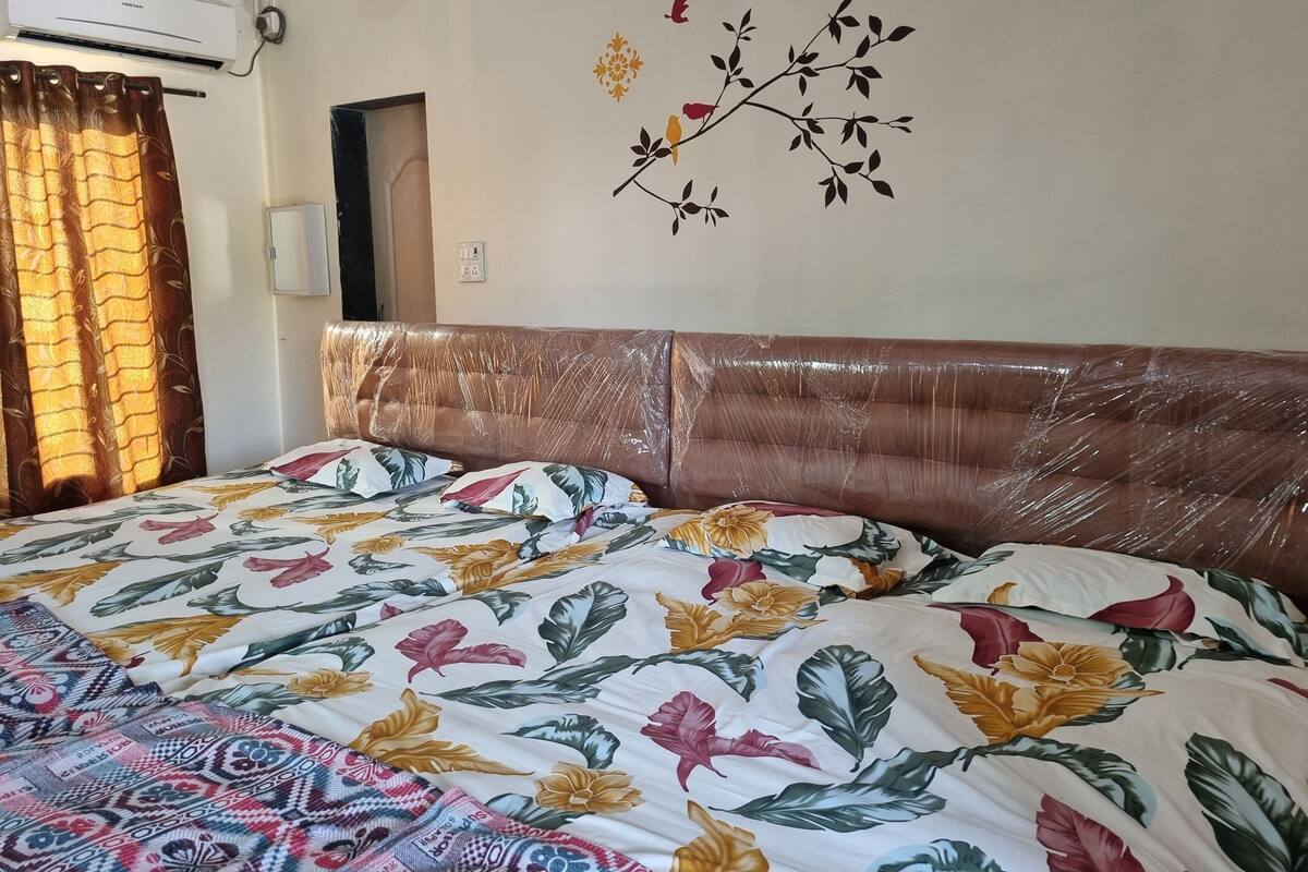 A room with a bed covered in floral bedding, a wall with a decorative branch and birds, and an air conditioning unit.