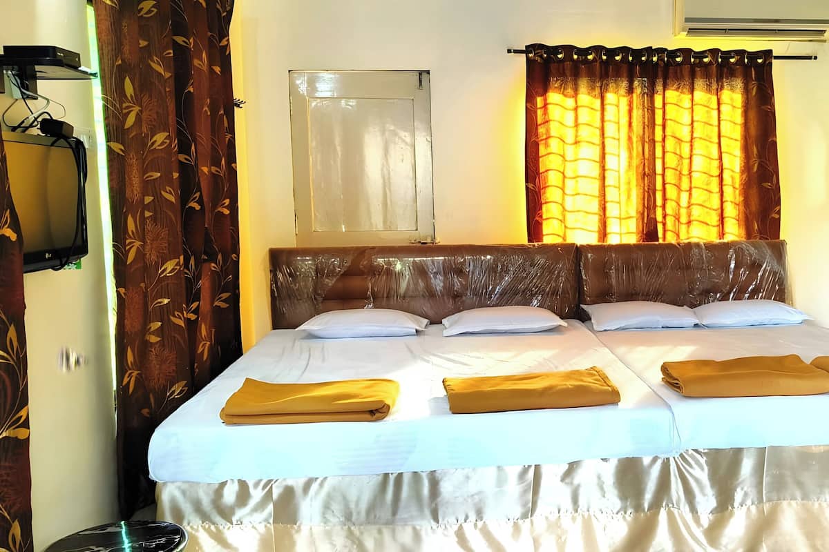 A double bed with two pillows and a blanket, a window with curtains, an air conditioning unit, and a wall-mounted light.