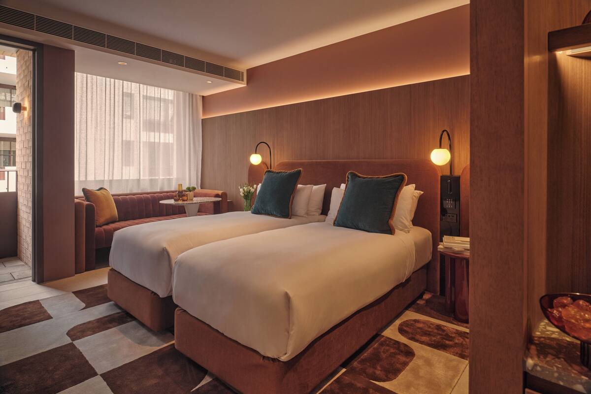 Ein Hotelzimmer mit zwei Betten, einem Sofa, einem kleinen Tisch und Blick auf die Stadt.
