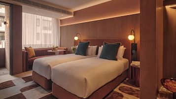 Ein Hotelzimmer mit zwei Betten, einem Sofa, einem kleinen Tisch und Blick auf die Stadt.