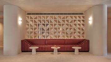 Un interno moderno con un divano rosso, due tavolini rotondi e un pannello murale geometrico.