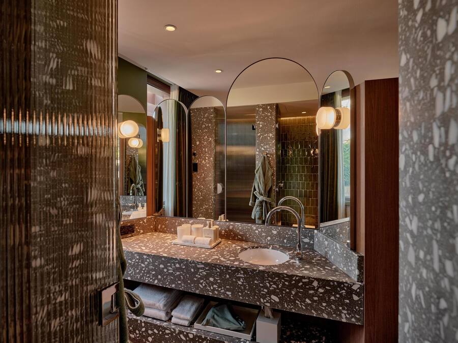 A modern bathroom with a granite countertop, a sink, and a large mirror. There are towels and a robe hanging on hooks.