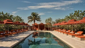 A pool area with lounge chairs and umbrellas, surrounded by trees and a clear sky. - The EVE Hotel Sydney (Redfern)