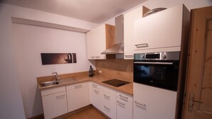 A modern kitchen with white cabinets, a wooden countertop, a sink, a coffee maker, and a built-in oven. - Ahornstein 6 Apartment (Embach)