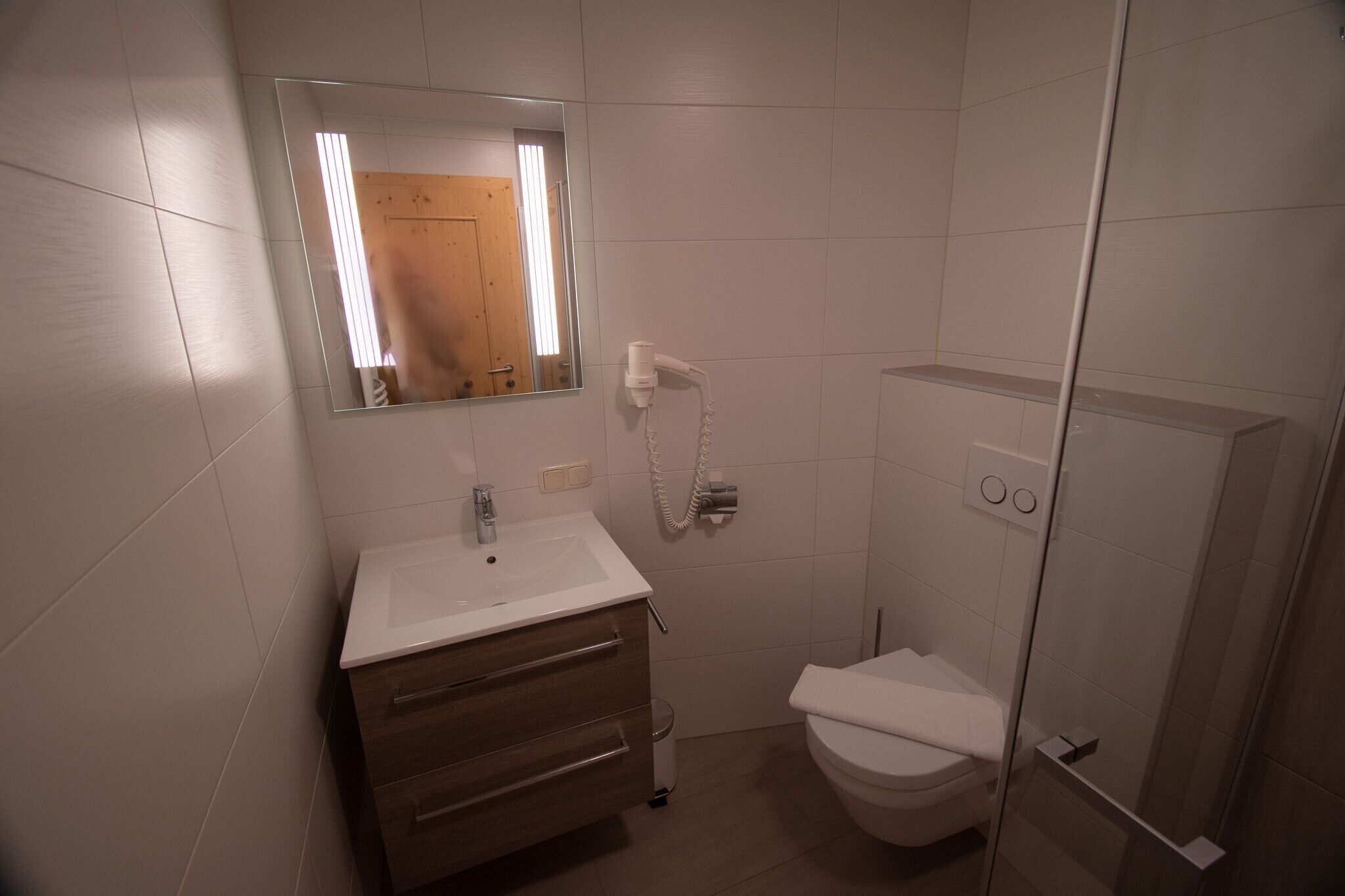 A bathroom with a white sink, a mirror, a toilet, and a shower area.